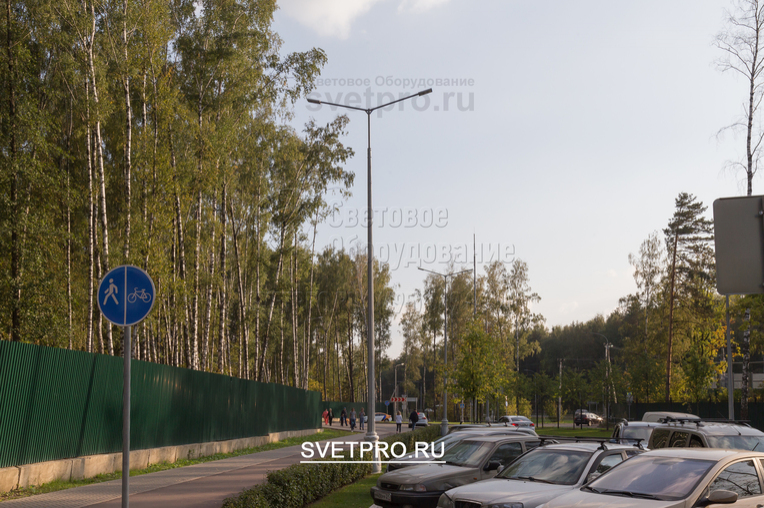 Установка кронштейнов со светильниками, которые светят в разные стороны от корпуса, позволяет с помощью одной инженерной конструкции осветить большое пространство. В примере на изображении опора освещает парковку для транспорта и пешеходную дорожку рядом с ней.