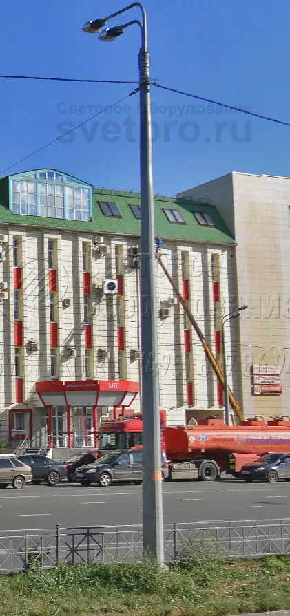 Опора, которая изображена на фото, может выдержать нагрузку до 1300 кг. Поэтому на ее верхушке установлено два световых прибора на кронштейне, а также подвешен силовой кабель и растяжка для крепления рекламных баннеров. Опора надежно закреплена на месте с помощью фланца и ЗДФ.
