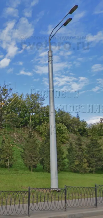 Опора на фотографии отличается повышенной несущей способностью. Поэтому на ее верхушке установлен кронштейн с двумя рожками, размещенными один над другим. Световые приборы создают яркое заливающее освещение, которого хватает для освещения тротуара и автомобильной дороги. 