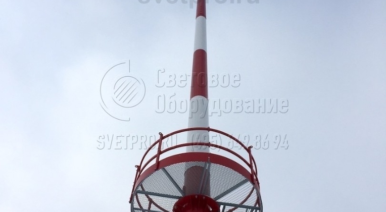 На этом изображении хорошо видна нижняя стационарная площадка и оголовок мачты. Оголовок осветительной конструкции имеет особую конструкцию. Он оснащен блоками, через которые пропускаются тросы для спуска подвижной рамы. Также на нем имеются замки для фиксации короны в верхнем положении.